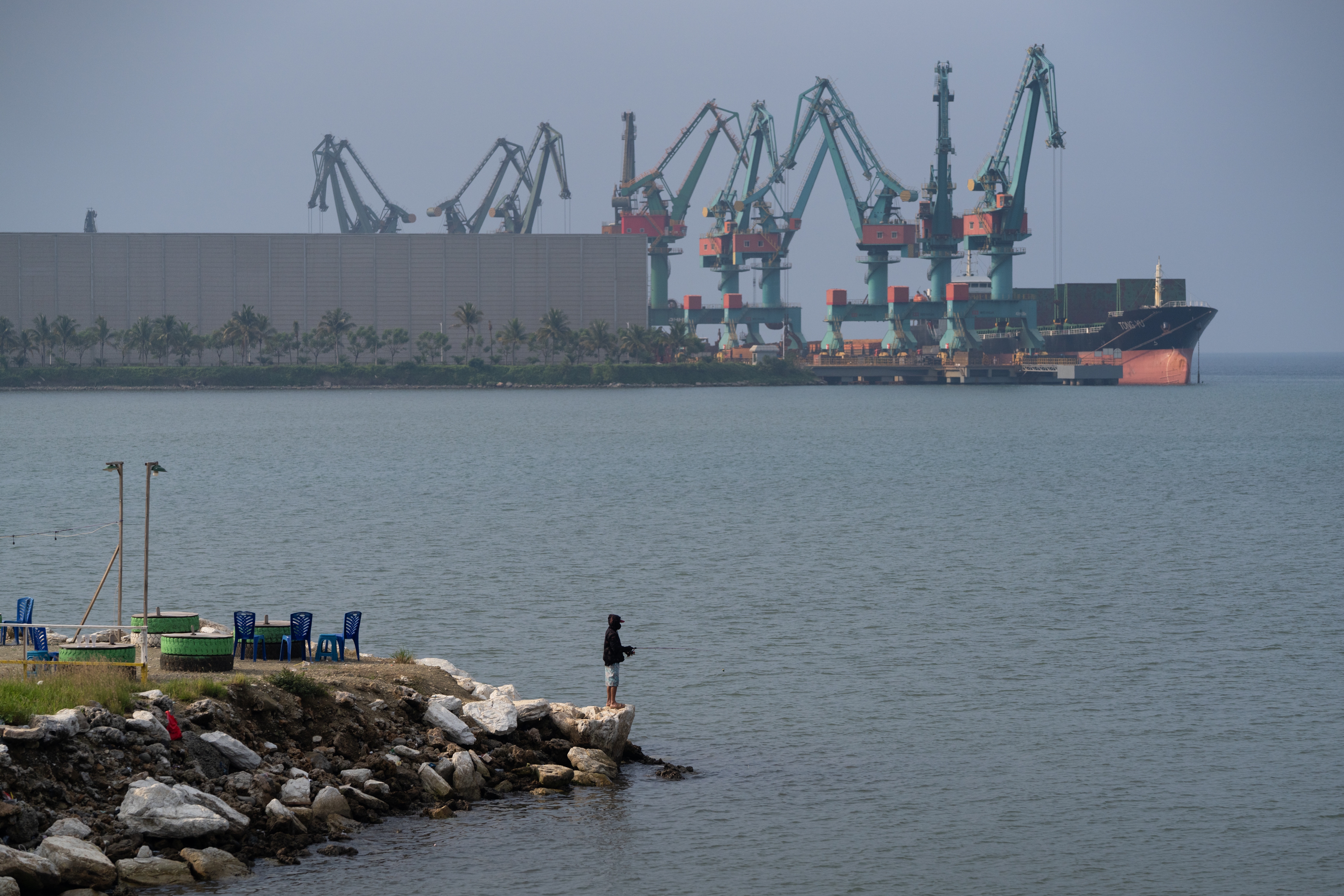 A man fishes next to shipping equipment  in Indonesia